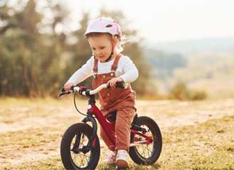 home 5 Toddler in helmet riding red balance bike.